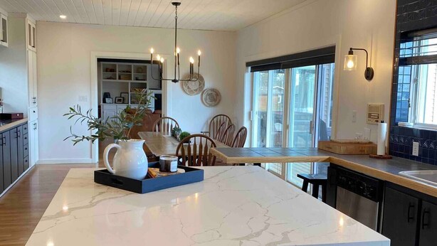 Et moderne køkken med en central ø, mørke skabe og et spiseområde med stole.