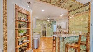 A kitchen with wooden shelves, a microwave, and a dining area with a glass-top table and chairs. - Rivers Edge: Spacious, Riverwalk, Close to USC, Ft Jackson, all area Hospitals (West Columbia)