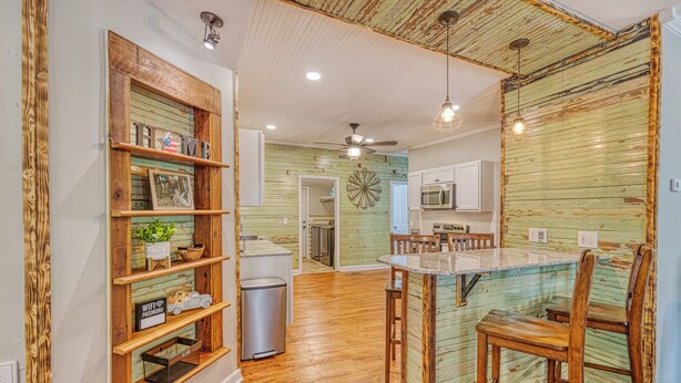 A kitchen with wooden shelves, a microwave, and a dining area with a glass-top table and chairs. - Rivers Edge: Spacious, Riverwalk, Close to USC, Ft Jackson, all area Hospitals (West Columbia)