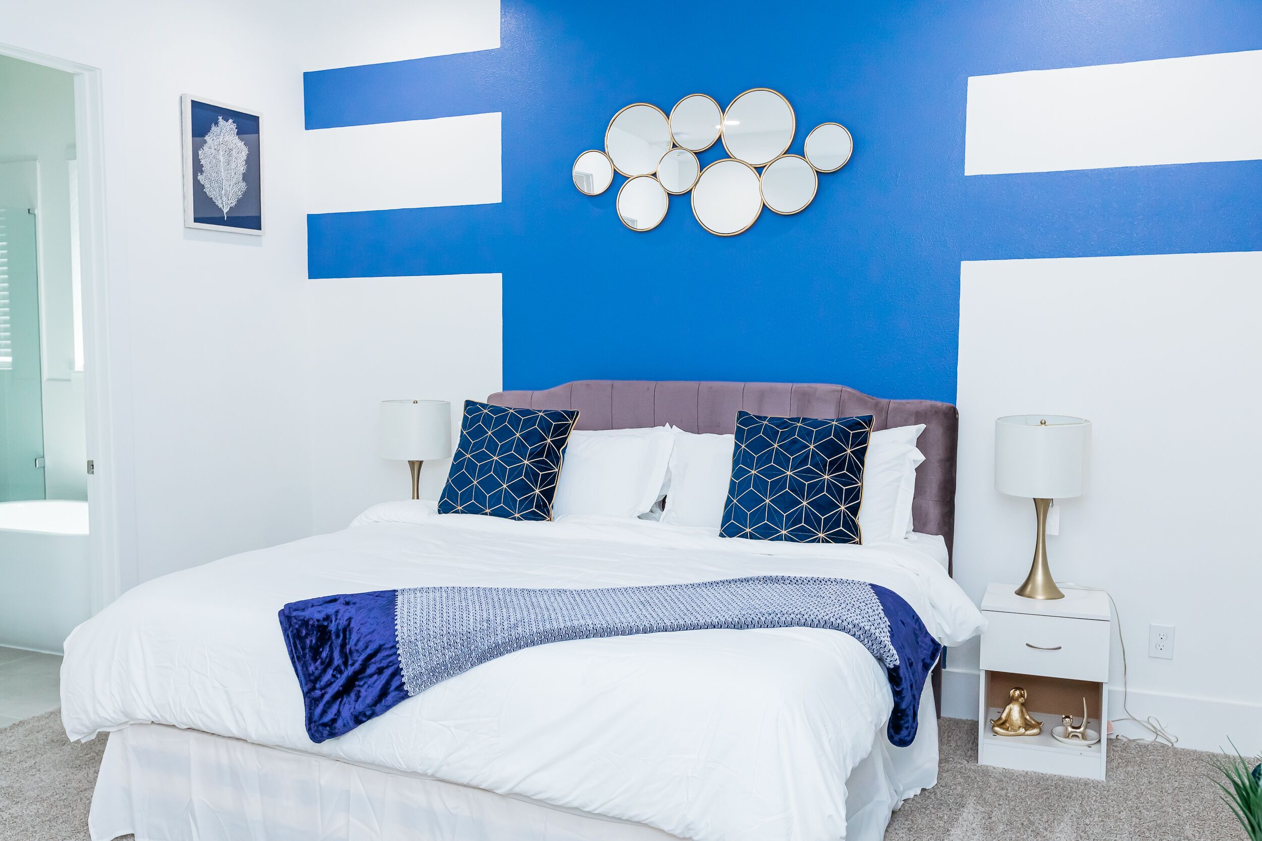 A modern bedroom with a large bed, blue and white decor, and a wall-mounted mirror.