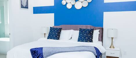 A modern bedroom with a large bed, blue and white decor, and a wall-mounted mirror.
