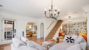A spacious living room with a large white sofa, a wooden staircase, and a bookshelf filled with books.