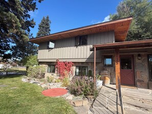 A two-story building with a stone facade, a wooden deck, and a red door. - Rizen Cottage - A Cozy Montana Getaway (Bozeman)