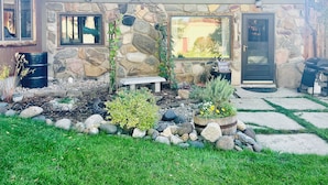 A stone facade with a stone bench, a garden with rocks and plants, and a sign reading "Rizen Cottage".