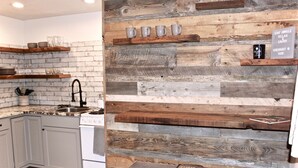 A kitchen with a rustic wooden wall, a sink, and various kitchen items on shelves.