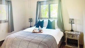 A bedroom with a bed, a ceiling fan, a nightstand, a window with curtains, and a bedside table.