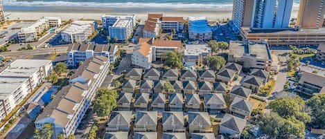 Vue aérienne d’un quartier résidentiel situé sur la côte, avec plusieurs immeubles d’appartements, une plage et un parking.
