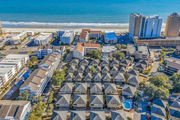 Vista aérea de uma área residencial costeira com vários edifícios de apartamentos, uma praia e um parque de estacionamento.