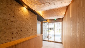 A modern reception area with a wooden reception desk, a textured ceiling, and a glass door leading outside. - GRAND BASE Nagasaki Nakamachi (Nagasaki)
