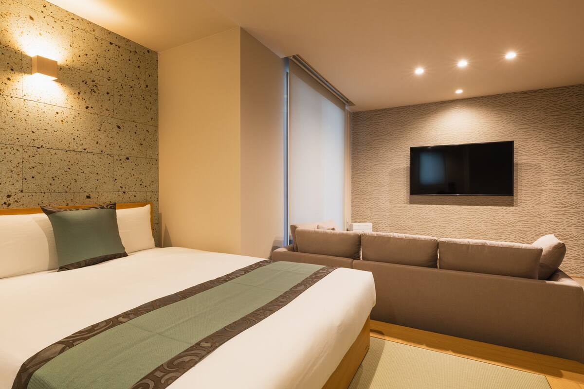A hotel room with a large bed, a sofa, a flat-screen TV mounted on the wall, and a textured wall.