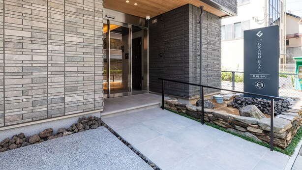A hotel entrance with a stone facade, a wooden ceiling, and a sign indicating the hotel name and location. - GRAND BASE Nagasaki Nakamachi (Nagasaki)