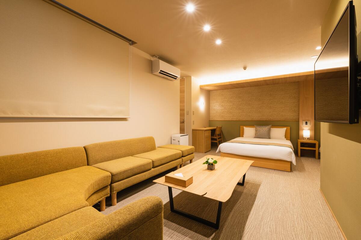 A modern hotel room with a sofa, a bed, a desk, and a flat-screen TV.