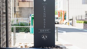 A black sign for the Grand Base Hotel with a logo and name in white. - GRAND BASE Nagasaki Nakamachi (Nagasaki)