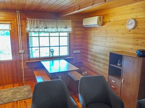 Interior de una cabaña de madera con una mesa de comedor, dos sillas, una ventana con vistas, un reloj y un equipo de aire acondicionado.