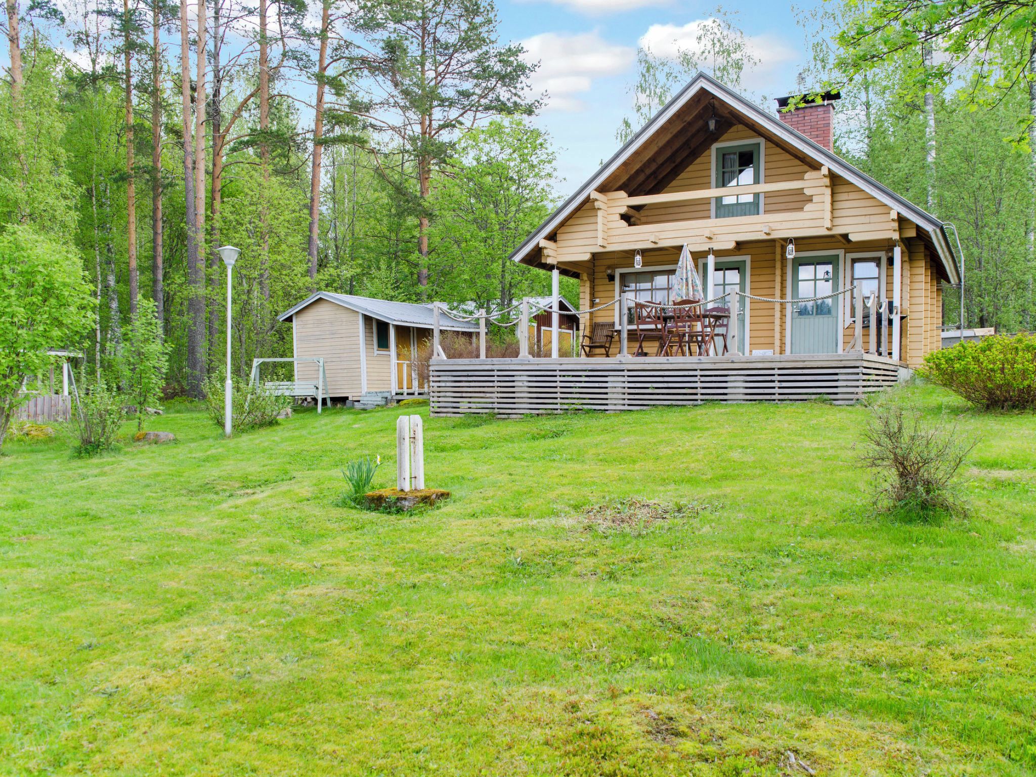 Puinen mökki, jossa on kuisti, ja sen ympärillä on nurmikko ja puita.