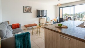 En moderne stue med sofa, sofabord og fjernsyn. Der er en balkon med bord og stole.