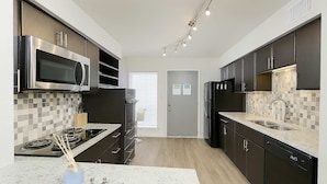 A modern kitchen with stainless steel appliances, a marble countertop, and dark cabinetry. - Royal Retreat | 2BR • 5 Min Walk to Galleria (Houston)