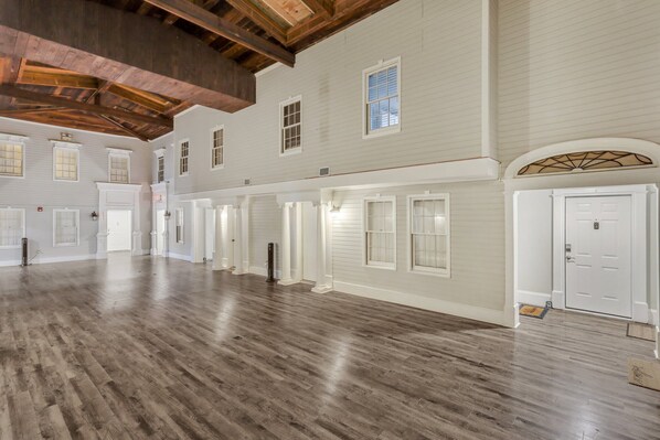 A spacious interior with a high ceiling and wooden beams, featuring multiple doors and windows along the walls.