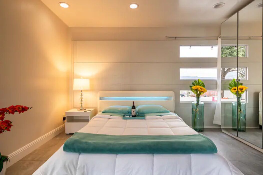 A modern bedroom with a bed, bedside table, lamp, and large windows.