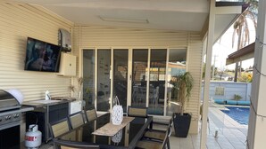 Une terrasse extérieure avec une table à manger, des chaises, un barbecue et une piscine.