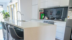Une cuisine moderne avec des meubles blancs, un îlot central et un réfrigérateur en acier inoxydable.