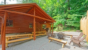 Un chalet rustique en rondins de bois, doté d’un patio couvert, de bancs en bois et d’un espace salon extérieur.
