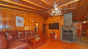 L’intérieur d’un chalet en bois est aménagé avec un canapé en cuir, une cheminée et un téléviseur fixé au mur.