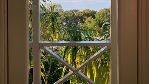 A view through a window with a white frame and decorative elements, overlooking a body of water and lush greenery. - Historic cottage with harbour views (Kohukohu)