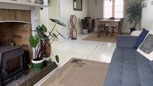 A cozy living room with a fireplace, a dining area, and a sofa. - Historic cottage with harbour views (Kohukohu)