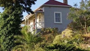 A two-story house with a red roof, a front porch, and a chimney. - Historic cottage with harbour views (Kohukohu)