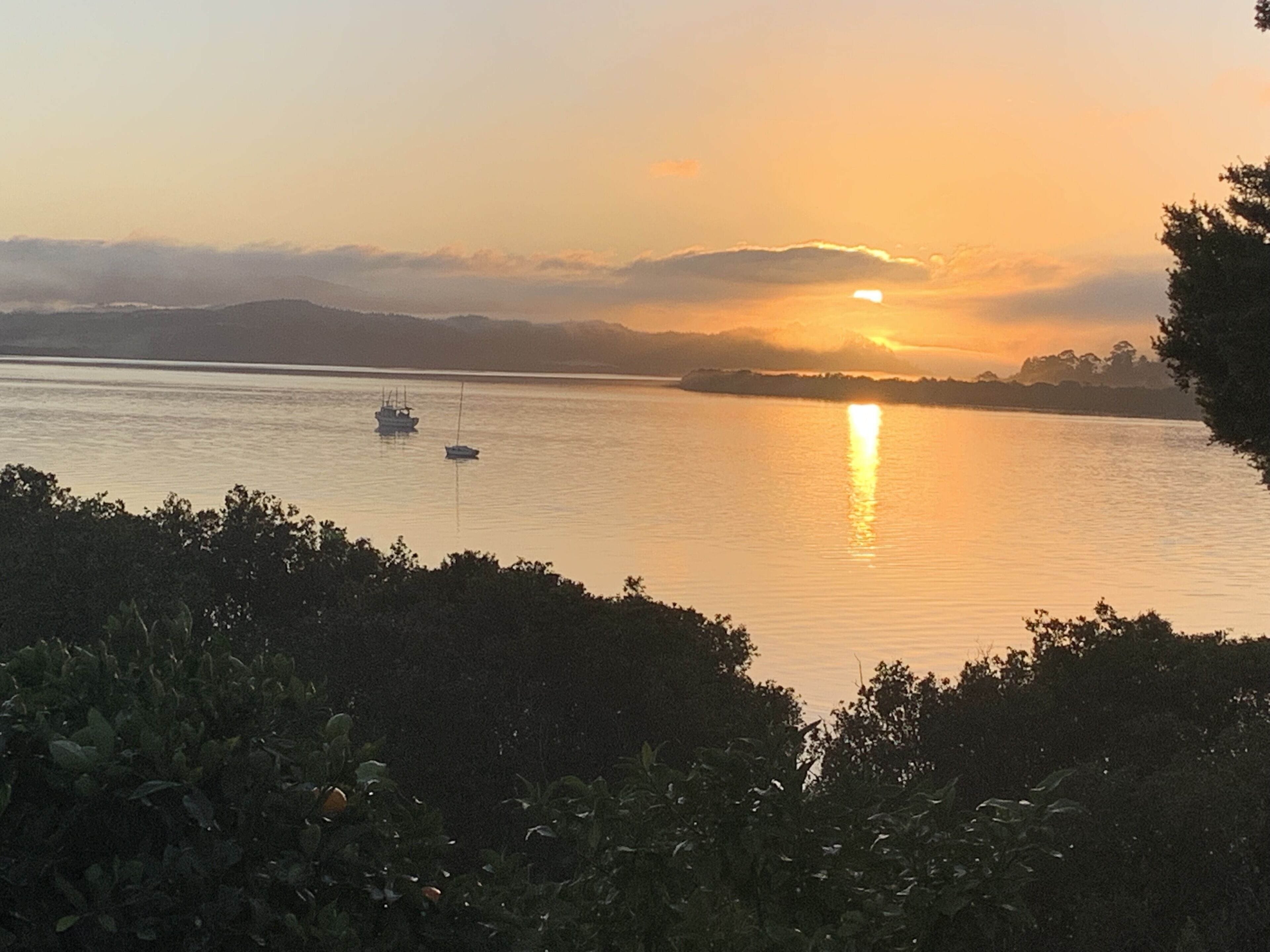 A sunset over a calm body of water with boats and distant land.