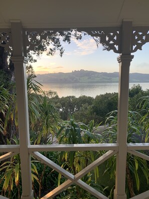 A view from a covered balcony with a pergola, overlooking a body of water and distant hills. - Historic cottage with harbour views (Kohukohu)