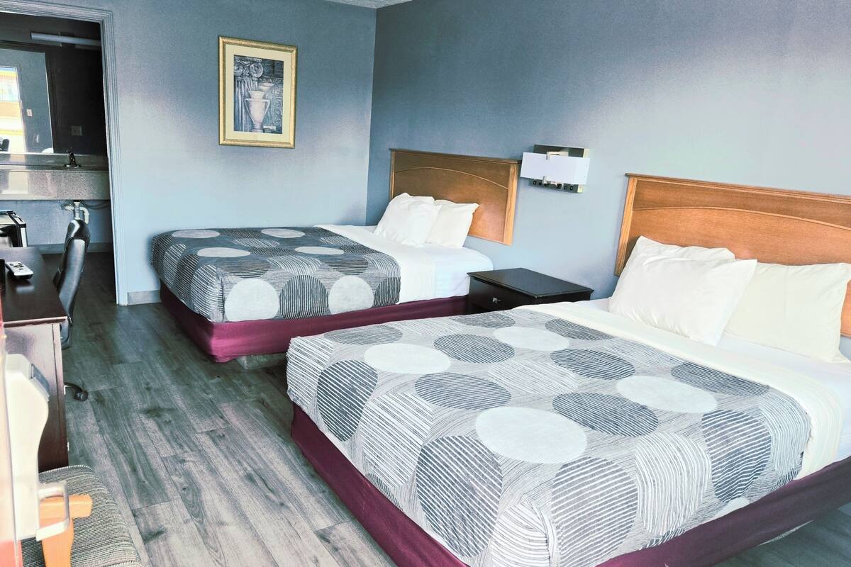 A hotel room with two beds, a desk, a chair, and a mirror.