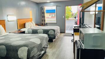 A hotel room with two beds, a desk, a television, and a window with curtains.