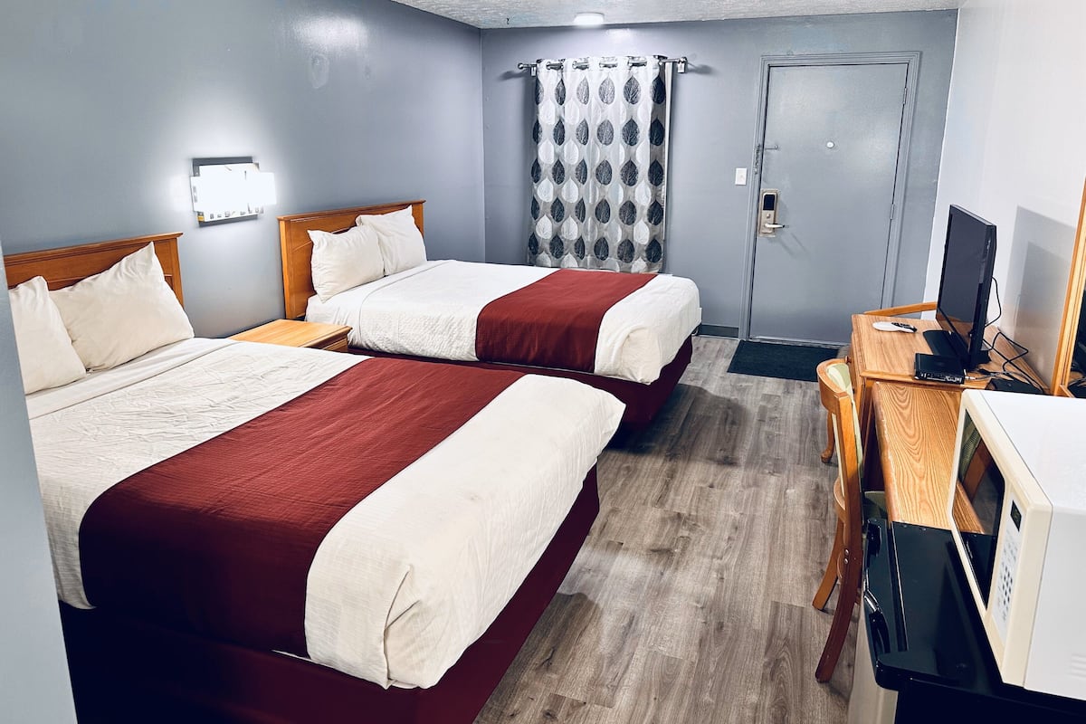 A hotel room with two beds, a desk with a computer, a microwave, and a door.