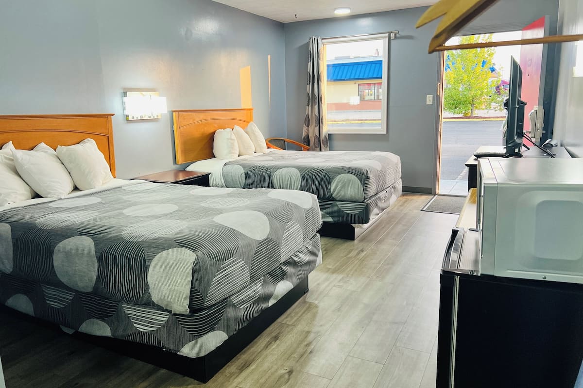 A hotel room with two beds, a desk with a computer, and a window with a view of the outside.