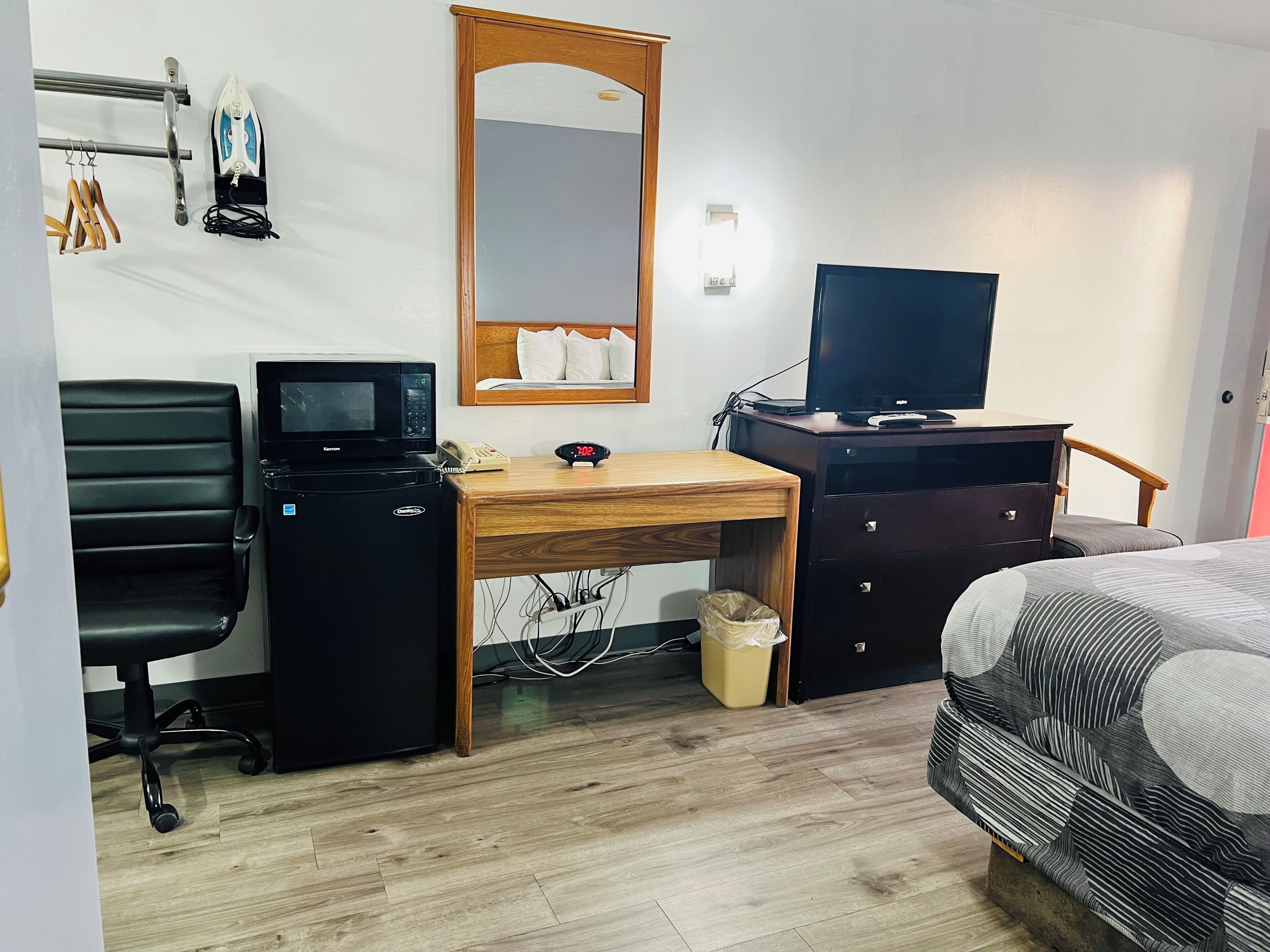 Una camera d'albergo con una scrivania in legno, una sedia da ufficio nera, un forno a microonde, una televisione, un letto con lenzuola a righe e uno specchio a parete.