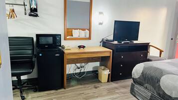 Una camera d'albergo con una scrivania in legno, una sedia da ufficio nera, un forno a microonde, una televisione, un letto con lenzuola a righe e uno specchio a parete.