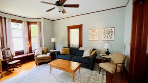 A living room with a dark green sofa, two armchairs, a wooden coffee table, and a ceiling fan. - Updated Victorian in the Heart of Sheboygan. Beach, Downtown, Golf, Road America (Sheboygan)