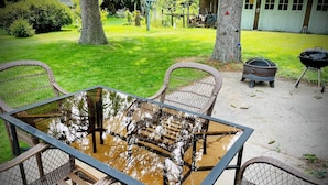 A glass-top table surrounded by wicker chairs in an outdoor setting with a grassy lawn, trees, and a barbecue grill in the background. - Updated Victorian in the Heart of Sheboygan. Beach, Downtown, Golf, Road America (Sheboygan)