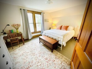 A bedroom with a bed, a desk, a chair, and a window.