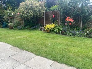 A well-maintained garden with a wooden fence, various flowering plants, and a green lawn.