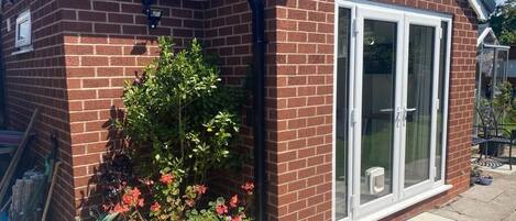 Casa de ladrillo con un gran ventanal corredero y un pequeño porche con plantas en macetas.