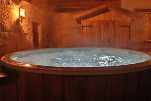 Ein Whirlpool in einem rustikalen Holzraum mit Steinwänden und Holzbalkendecke.