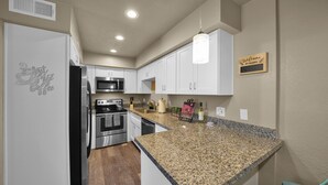 A kitchen with white cabinets, stainless steel appliances, granite countertops, and a welcome sign. - Heart of Scottsdale (Scottsdale)