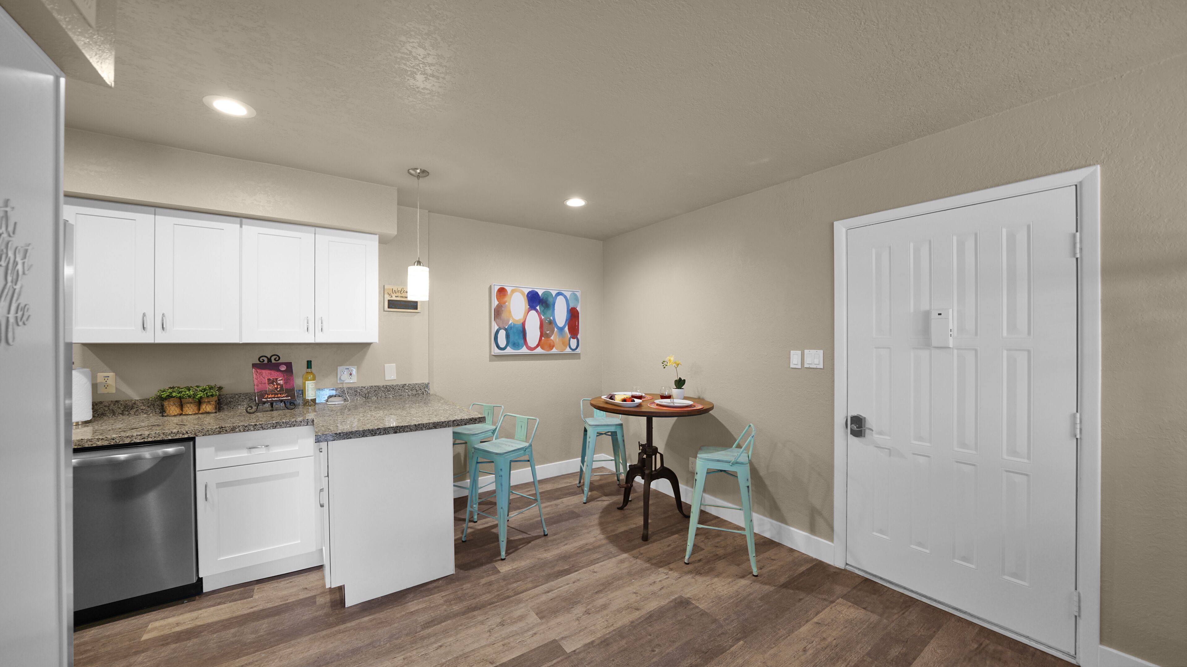 Une cuisine compacte avec des meubles blancs, un plan de travail en granit et un coin repas doté de chaises turquoise.