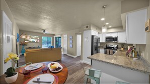 A modern kitchen with granite countertops, stainless steel appliances, and a dining area with a wooden table and chairs. - Heart of Scottsdale (Scottsdale)