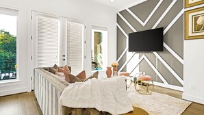 A modern living room with a sectional sofa, a flat-screen TV mounted on the wall, and a large window with blinds. - Luxury Houston Downtown townhome Minute Maid/Toyota/ Medical center (Houston)