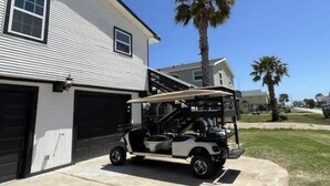 Een golfkarretje geparkeerd voor een huis met een garage en een palmboom op de achtergrond.