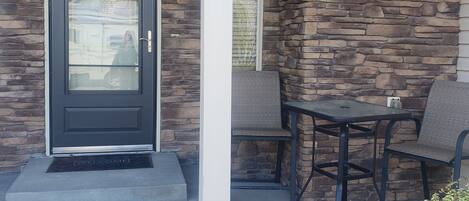 A stone exterior with a dark door, a small outdoor seating area with two chairs, and a welcome mat at the entrance.